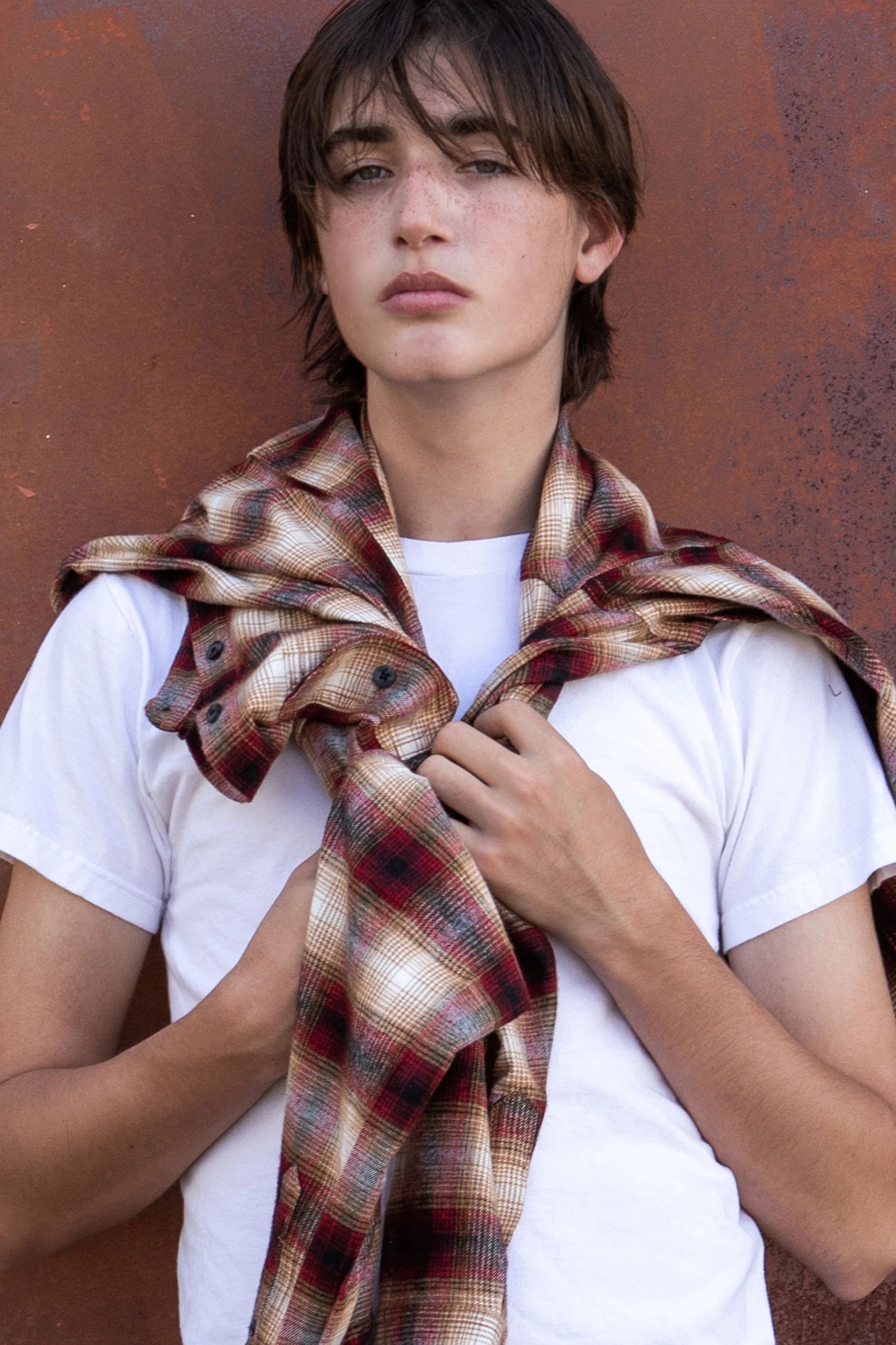 Teen wearing a white t-shirt with a plaid shirt draped over shoulders.