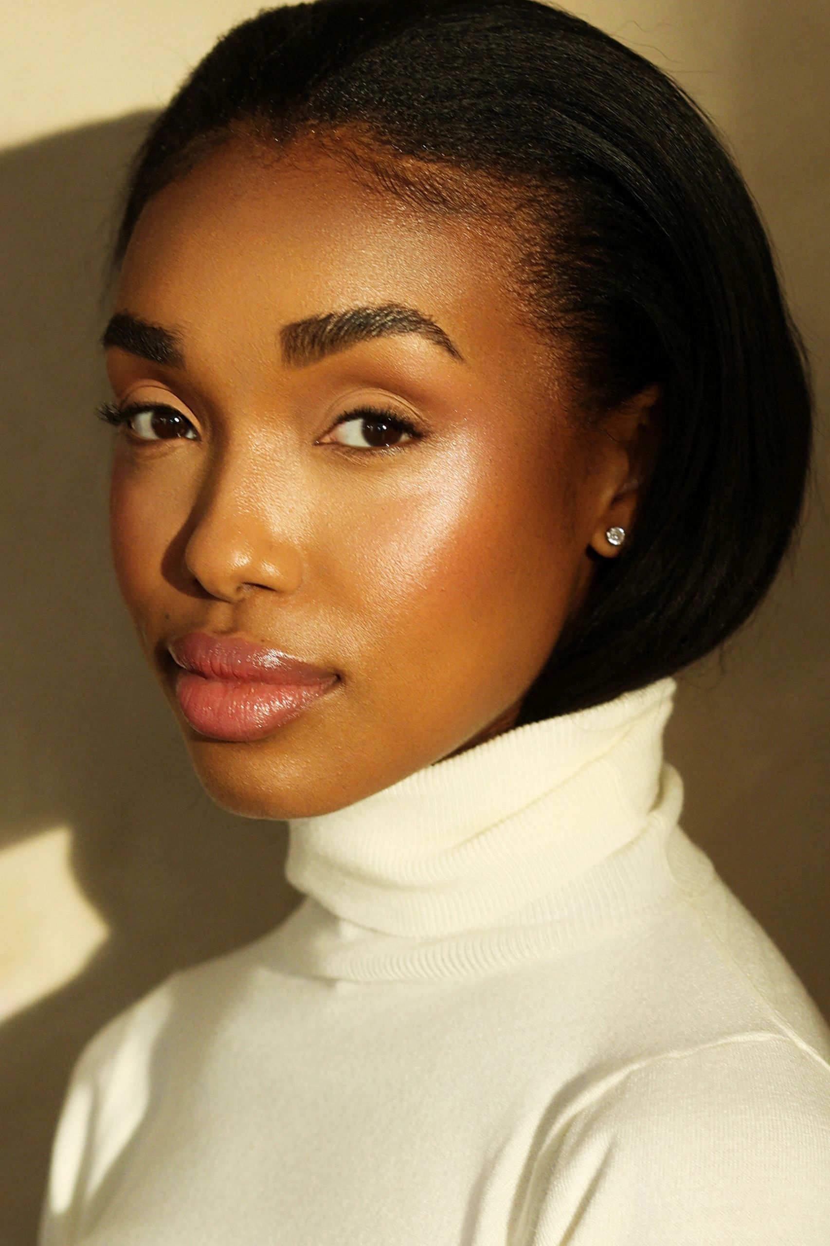 Close-up portrait of a woman in a white turtleneck with glowing skin.