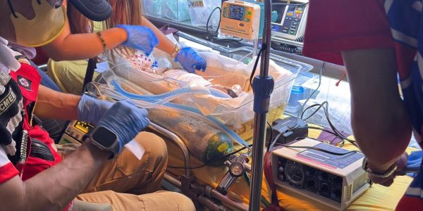 Medical personnel attending to a newborn in an incubator inside an ambulance.