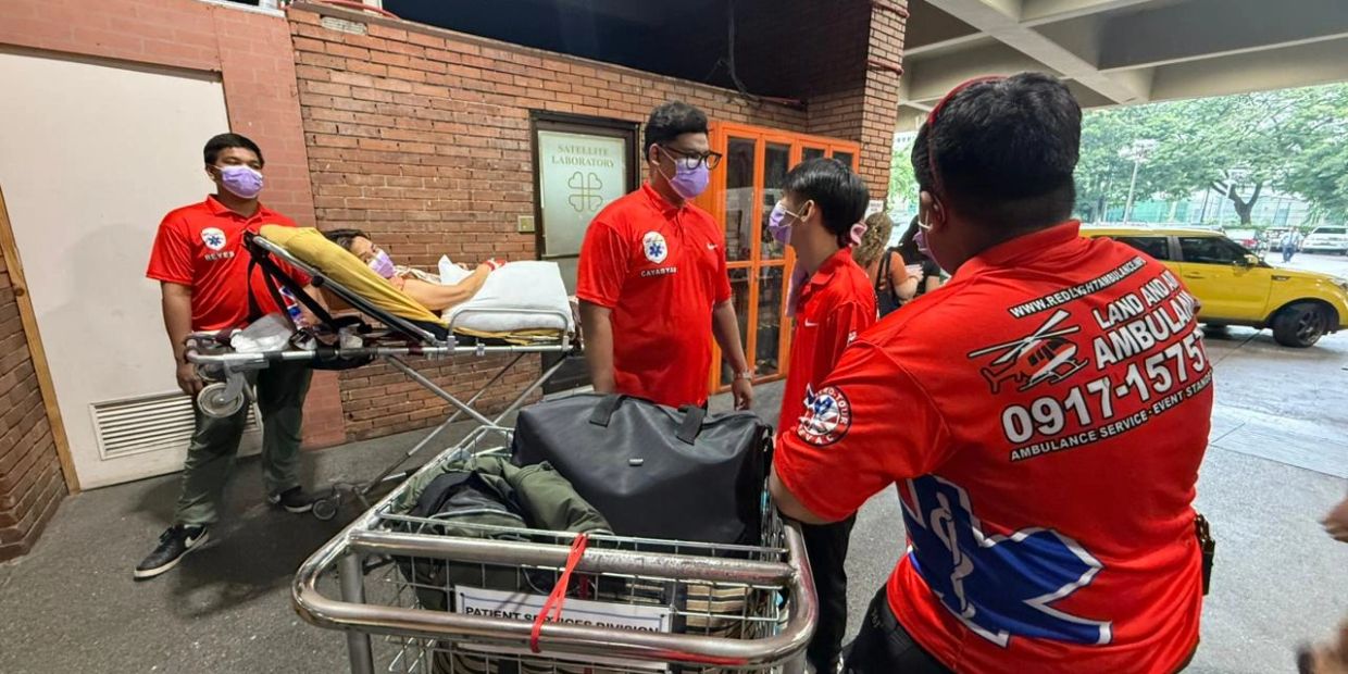 Emergency responders in red uniforms assist a patient on a stretcher outside a hospital.