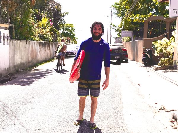 Man in swimwear holding a red surfboard on a sunny street.