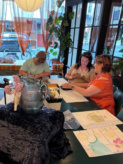 Three women engaged in art and crafts at a table near a window.