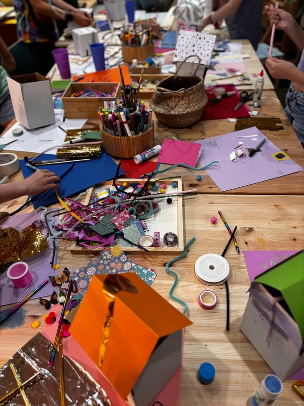 A busy craft table filled with colorful supplies and hands working on projects.
