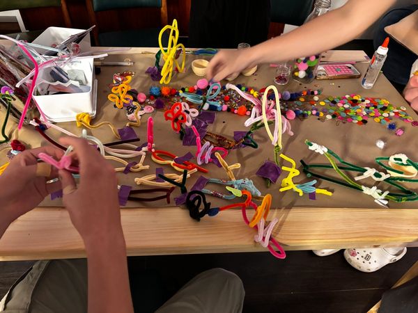 Hands crafting colorful pipe cleaner shapes and decorations on a cluttered table.
