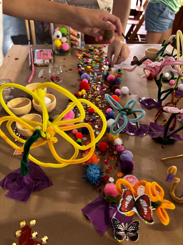 Children's hands decorating a table with colorful craft materials and pipe cleaner flowers.