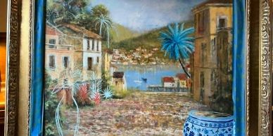 Framed painting of a coastal village with buildings and a calm sea.