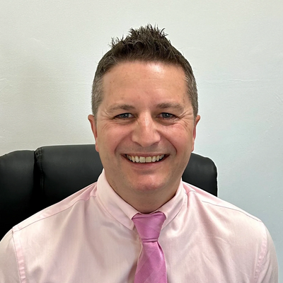 Smiling man in a pink shirt and tie sitting in an office chair.