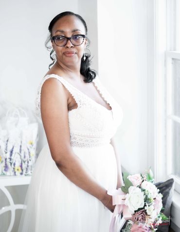 Woman in a white dress holding a bouquet near a window.