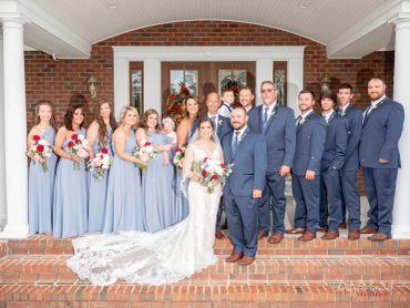A wedding party poses on brick steps in front of a house.