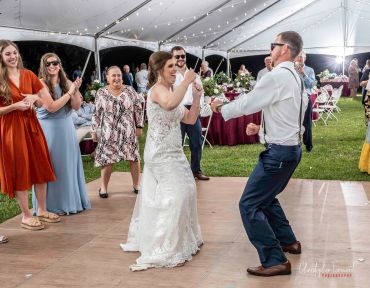 Bride and groom dancing with guests at outdoor wedding.