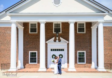 Wedding couple poses in front of a building with large columns.