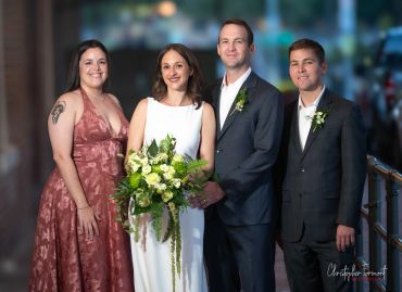 Group portrait of two women and two men, with a bride holding flowers.