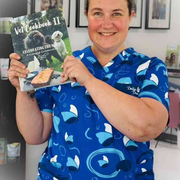 Person holding Vet Cookbook II book and smiling.