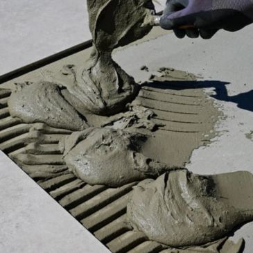maniobra de albañilería para poner un abaldosa, con cemento gris 