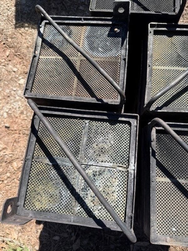Close-up of stacked black metal trays with mesh bases and handles.