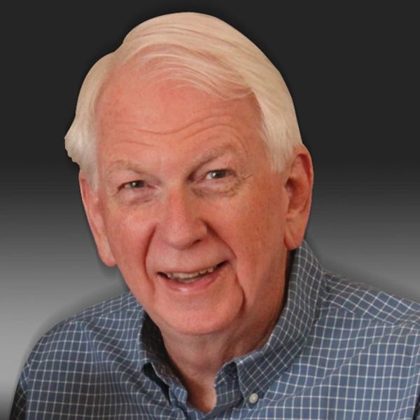 Smiling elderly man with white hair wearing a blue checkered shirt.