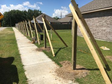 Temporary wooden supports brace a new fence line along a sidewalk.