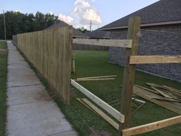 Partially built wooden fence along a sidewalk beside a house.
