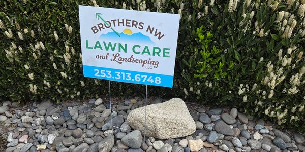 A lawn care sign placed among rocks and shrubs.