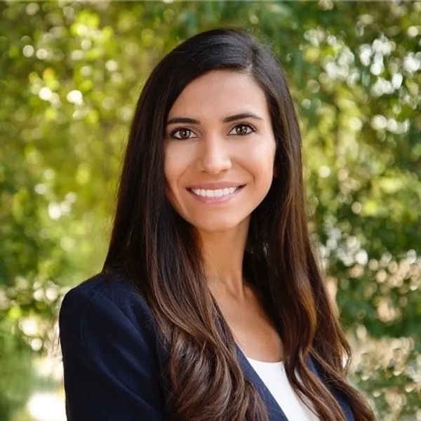 Professional woman with long dark hair smiling outdoors.