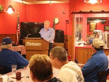 A man speaks at a podium in a cozy restaurant with an attentive audience.