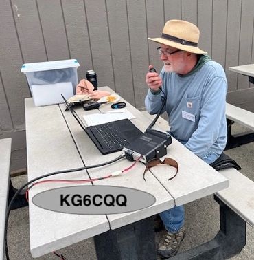 Man operating ham radio equipment at picnic table outdoors.