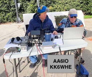 Two men operating radio equipment at a table outdoors.