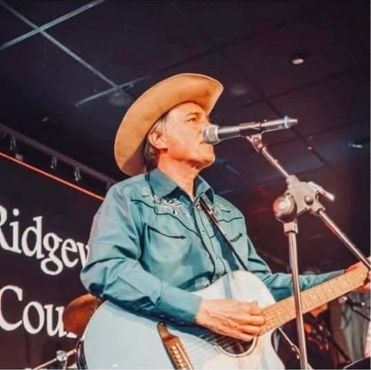 Musician in cowboy hat playing guitar and singing on stage.