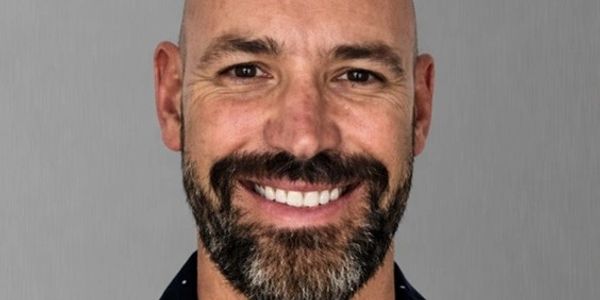 Smiling bald man with a beard against a gray background.