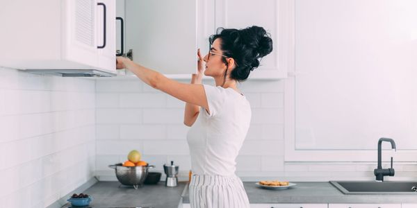 Woman reaching into a kitchen cabinet in a bright, modern kitchen.
