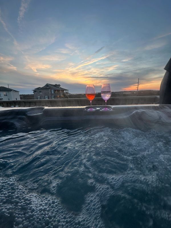 Two glasses of wine on a hot tub edge at sunset with houses in the background.