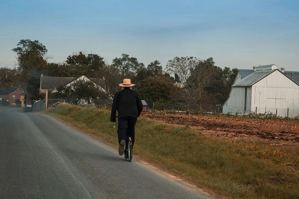 Experience the charm of Lancaster County, Pennsylvania, home to the largest Amish community in the U.S. This serene image captures an Amish man riding a scooter down a peaceful country road, surrounded by historic barns and rolling farmland. Lancaster offers a unique cultural experience, where visitors can explore local markets, scenic backroads, and traditional Amish crafts while respecting the simplicity of Amish life. Plan your visit to Lancaster County and immerse yourself in the beauty of Pennsylvania Dutch Country.