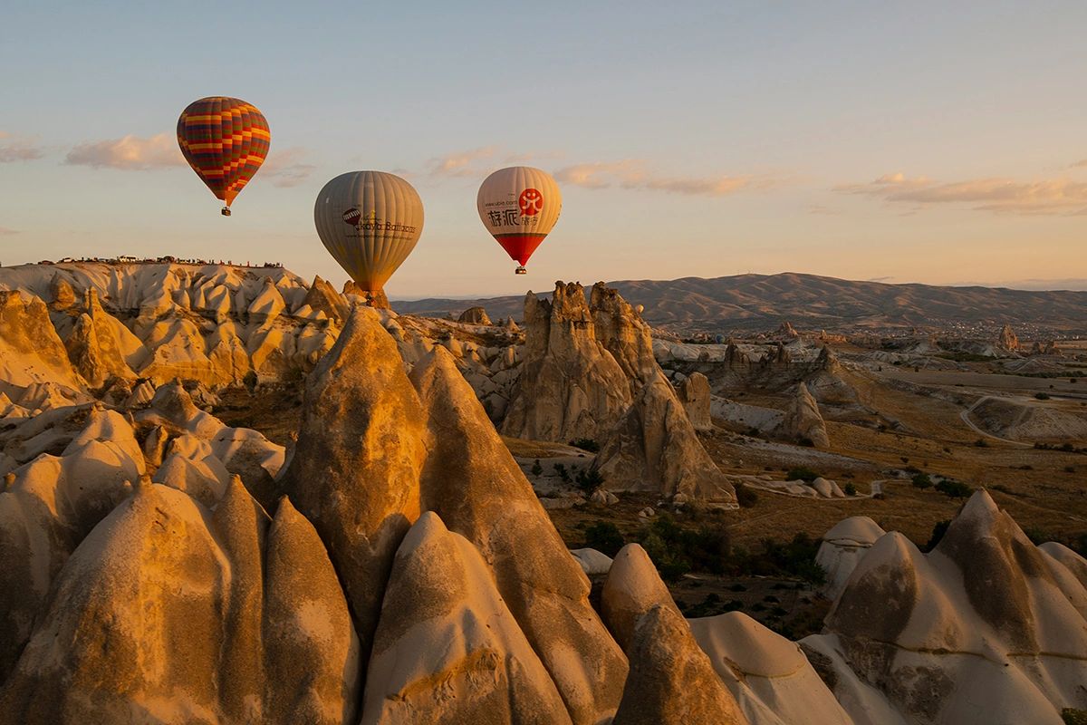 Multiple colorful hot air balloons floating over Cappadocia fairy chimneys and rock formations at golden hour sunrise