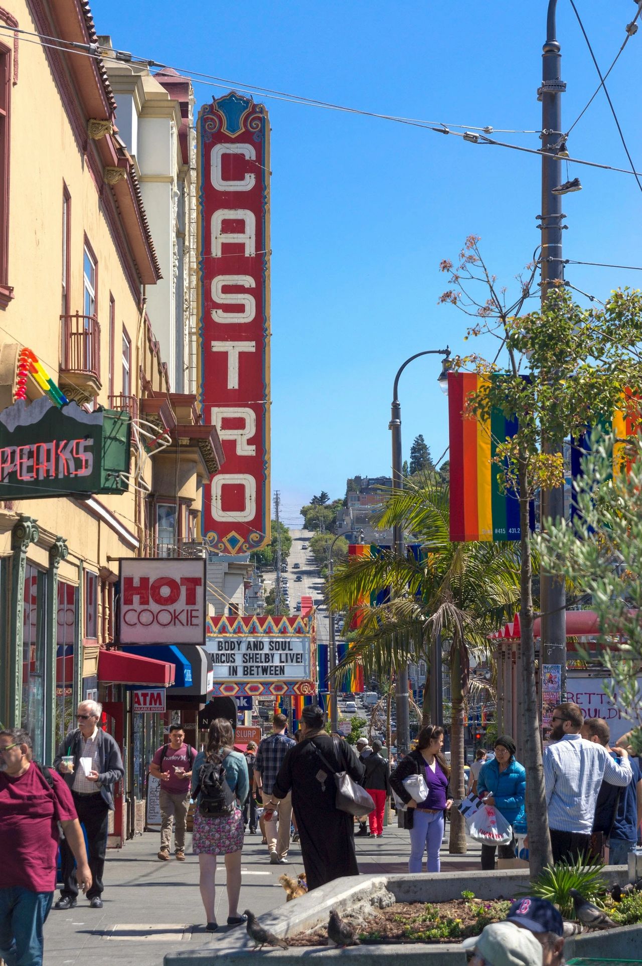 Castro Theatre neon sign reading "CASTRO" with rainbow flags and "Hot Cookie" shop on bustling San Francisco street – essential San Francisco guide stop