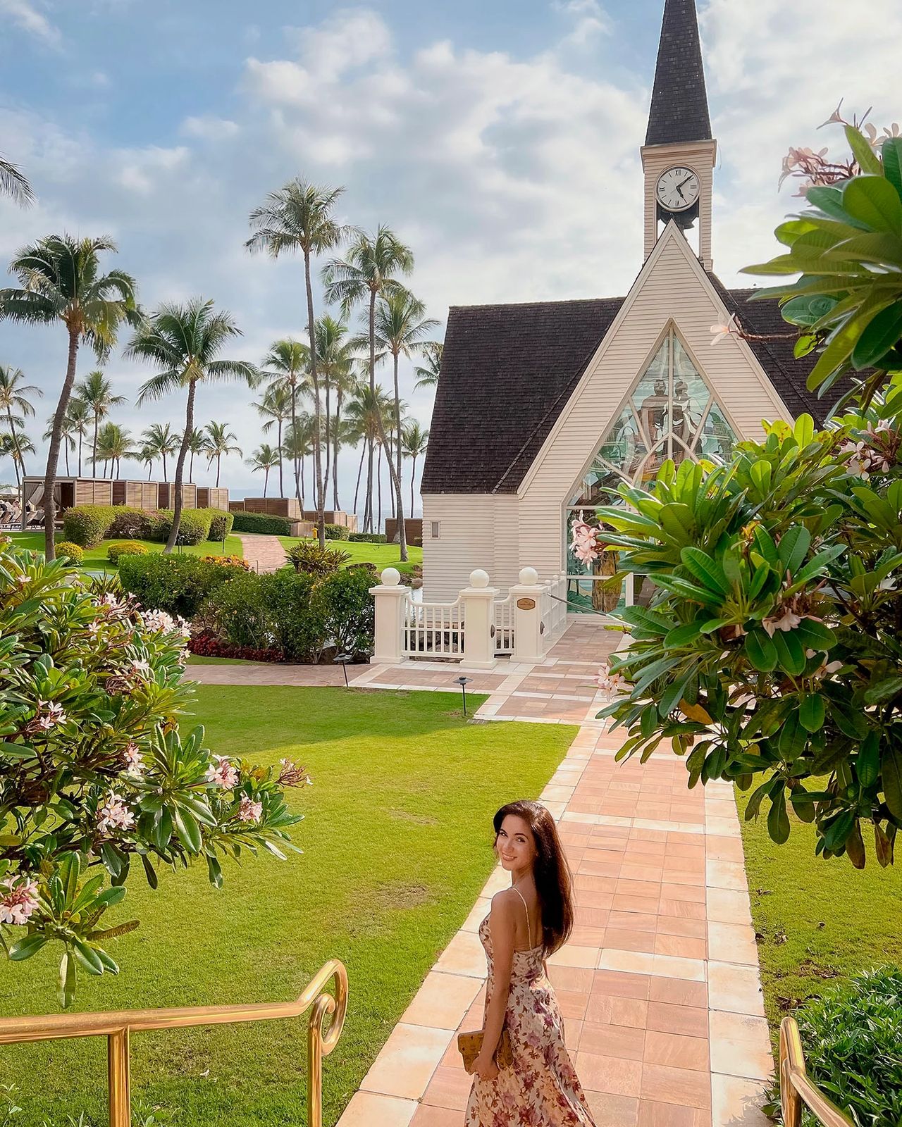 Woman in floral dress walking toward white wedding chapel surrounded by tropical gardens at Grand Wailea Maui
