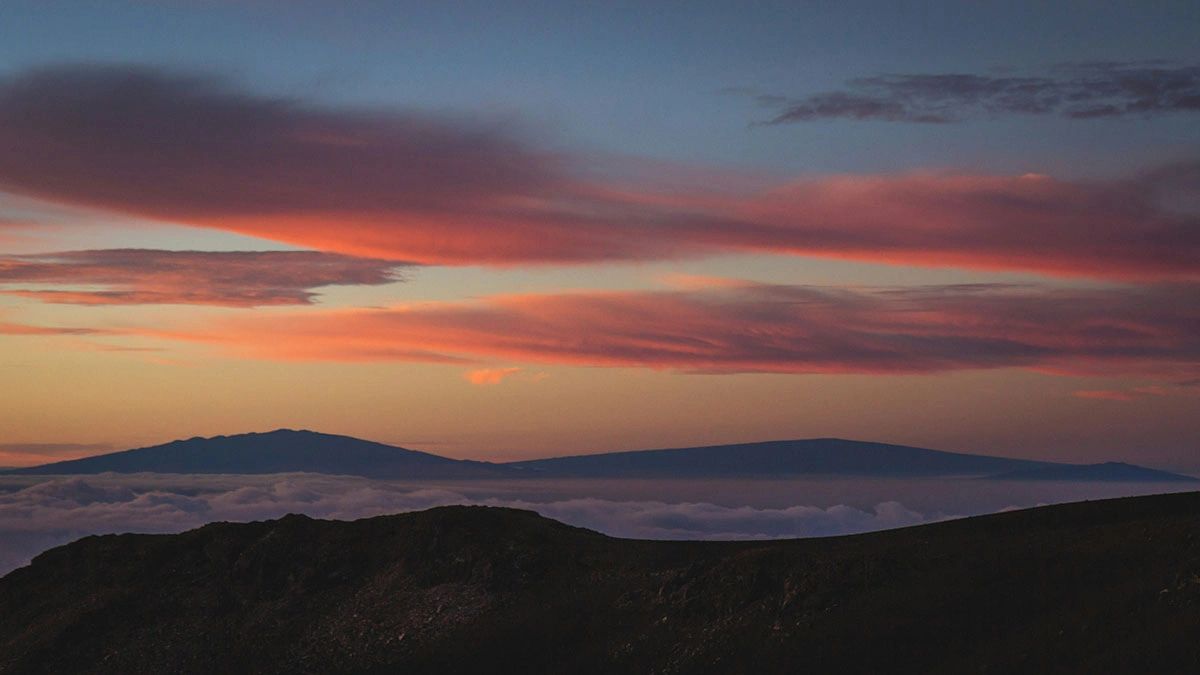 Dramatic sunrise with pink and orange clouds above Haleakalā Summit, a must-do experience on any Maui travel guide