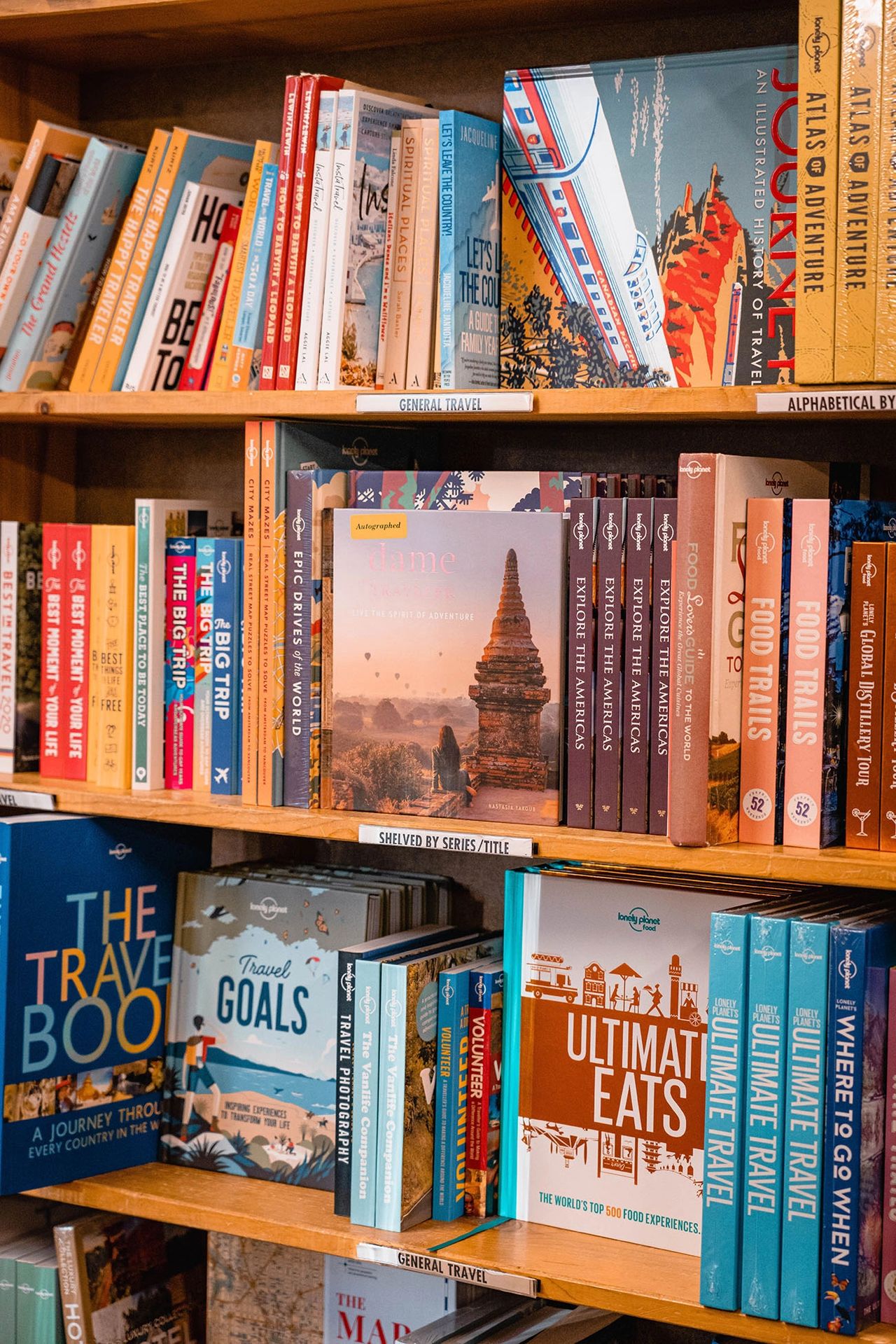 A colorful bookshelf display inside Powell’s City of Books in Portland, Oregon, featuring a variety of travel books, including Dame Traveler: Live the Spirit of Adventure by Nastasia Yakoub alongside Lonely Planet guides and inspirational titles. This iconic independent bookstore is located in the Pearl District and is a must-visit destination for book lovers and travelers exploring Portland. Photo by Nastasia Yakoub