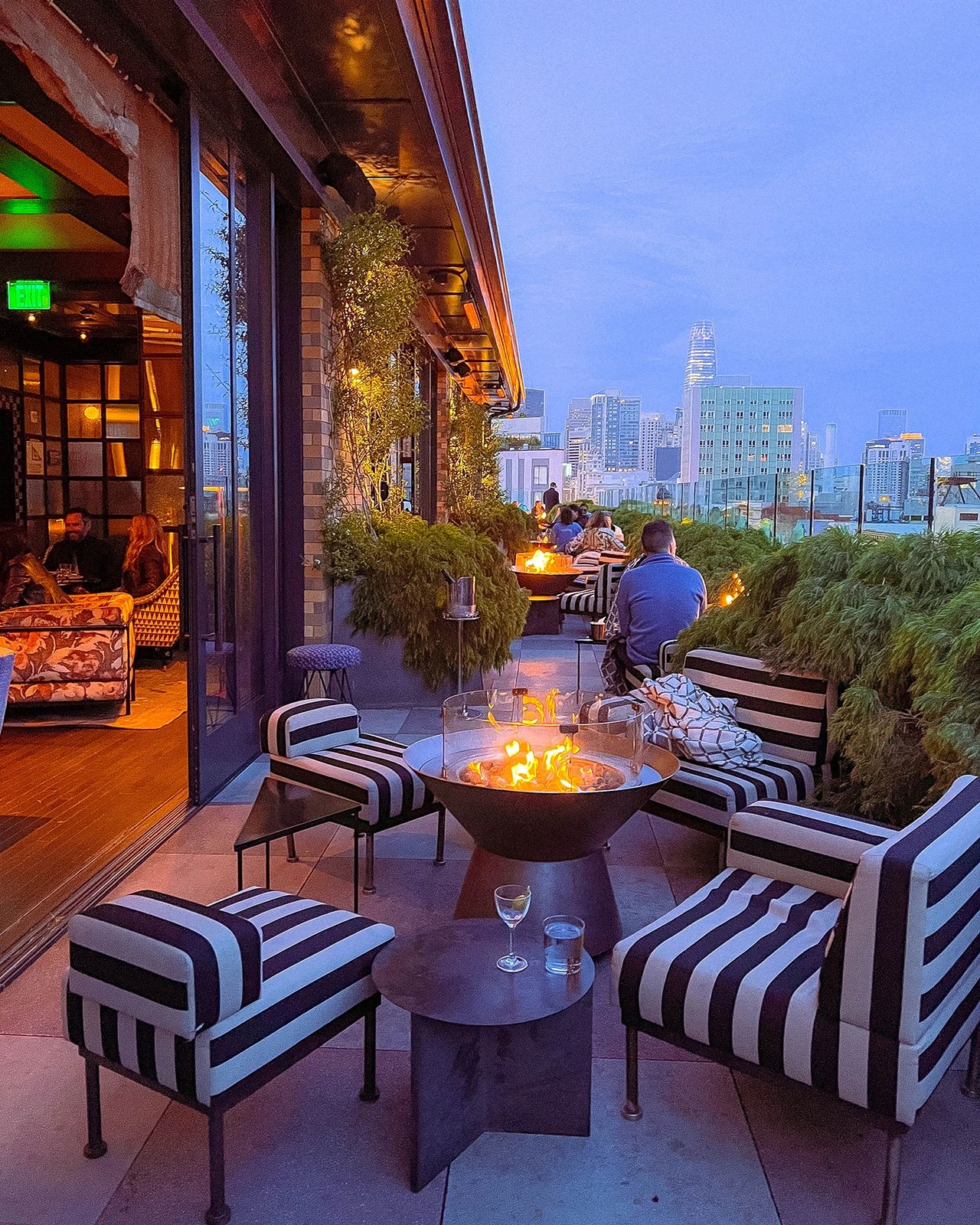 Chic rooftop evening at Charmaine’s Rooftop Bar at the San Francisco Proper Hotel, featuring striped lounge chairs, cozy fire pits, and sweeping views of the city skyline. Perfect for cocktails at sunset or nighttime gatherings, Charmaine’s offers one of the best rooftop experiences in San Francisco with stylish decor and an upscale yet relaxed atmosphere.