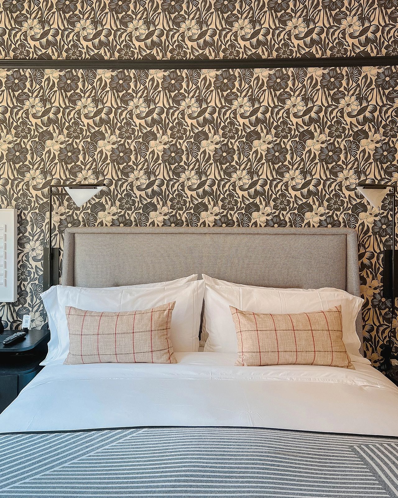 Stylish guest room at the San Francisco Proper Hotel, featuring a chic upholstered headboard, crisp white bedding, patterned throw pillows, and a bold floral wallpaper backdrop. Known for its eclectic design and luxurious boutique feel, the Proper Hotel offers a unique and elegant stay in the heart of San Francisco.