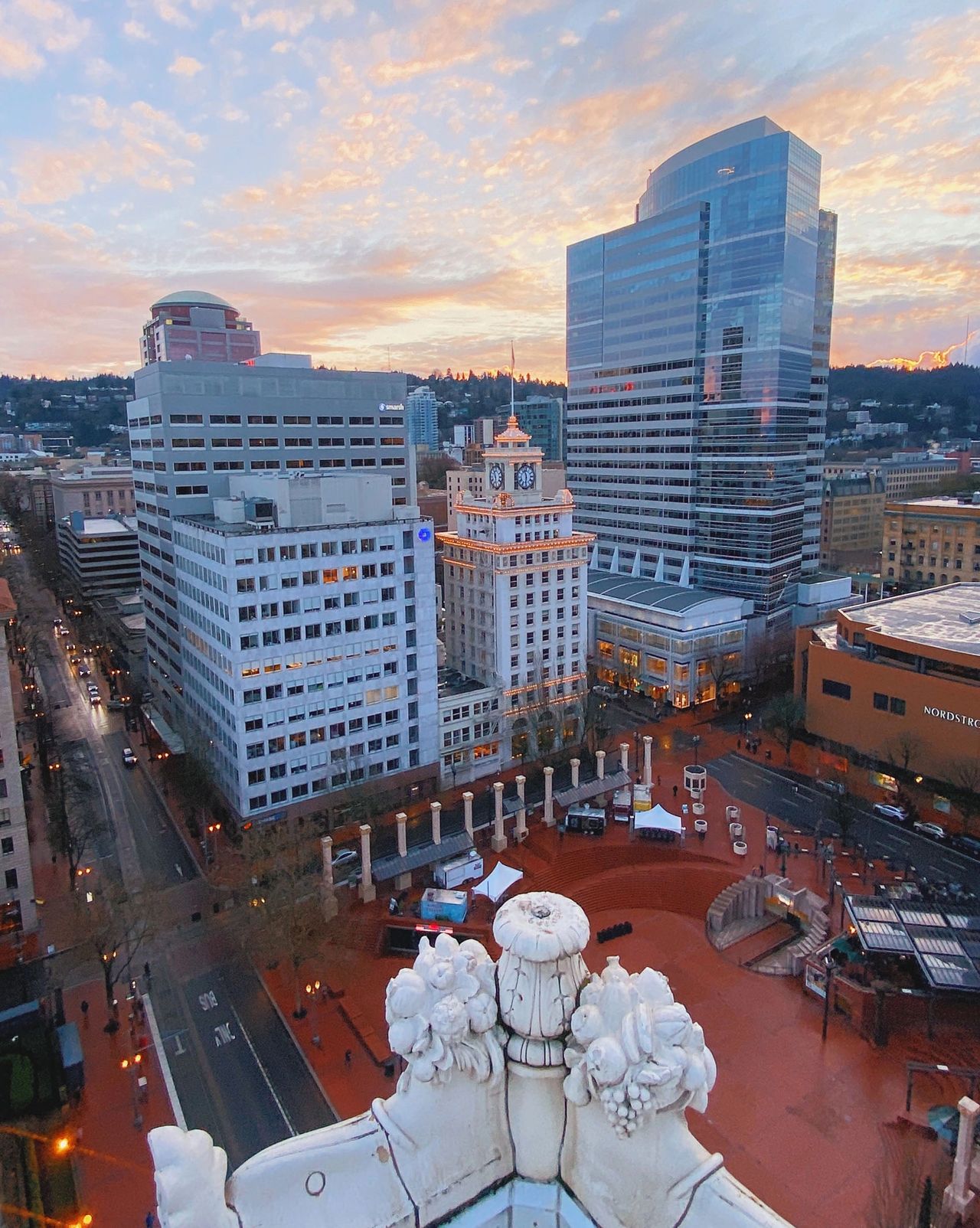 A panoramic sunset view over downtown Portland, Oregon, taken from the rooftop of The Nines Hotel. The scene overlooks Pioneer Courthouse Square, historic clocktower buildings, and modern high-rises against a backdrop of pastel-colored skies. This elevated perspective highlights the mix of historic architecture and contemporary design that defines Portland’s cityscape, making The Nines a prime spot for scenic views and luxury stays in the heart of downtown. Photo by Nastasia Yakoub
