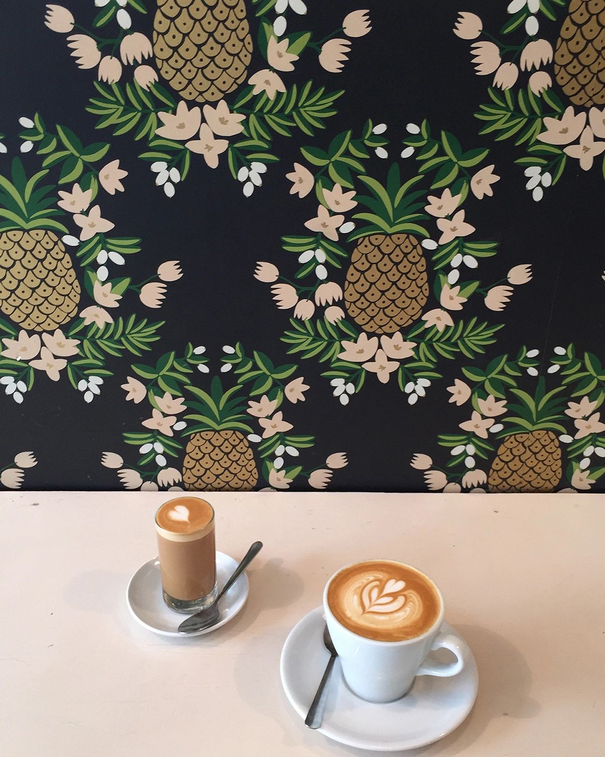 Two artisan lattes at Wrecking Ball Coffee Roasters in San Francisco, set against the café’s signature pineapple-patterned wallpaper. Known for its expertly crafted coffee and playful design, Wrecking Ball is a beloved local favorite for specialty coffee lovers seeking a cozy and photogenic spot in the city.