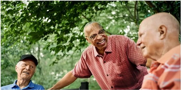 Three elderly men joyfully socializing outdoors under green trees.