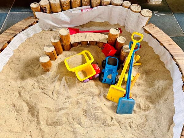 Children's sandpit with colorful plastic toys and bamboo border.