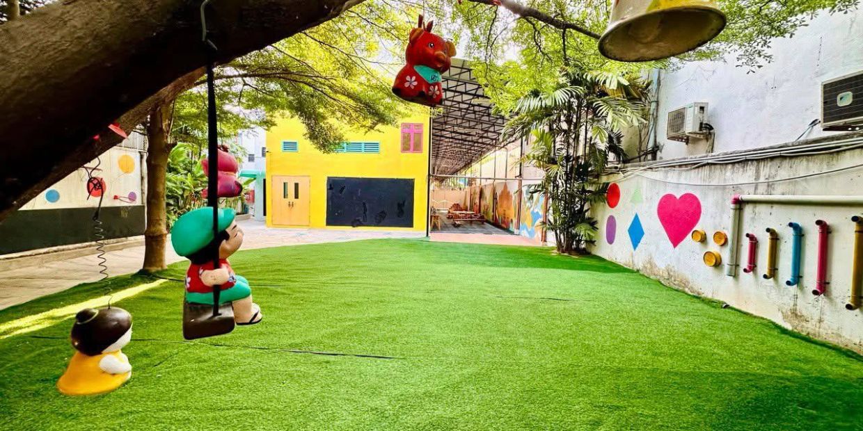 Colorful playground with swings, vibrant wall art, and lush greenery under large trees.