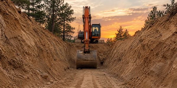 Excavator digging trench at sunset.