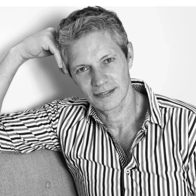 Man in a striped shirt leaning on a couch, smiling gently.