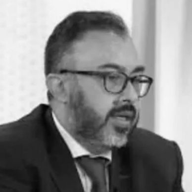 Man with glasses and beard in a suit speaking.