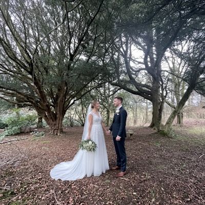 Bride and groom standing in a forest, holding hands and looking at each other.