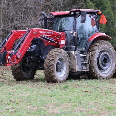 Red tractor with muddy tires parked on a grassy field.