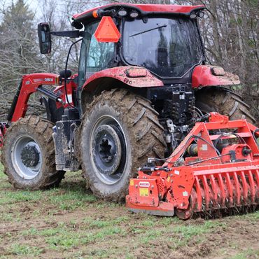 Red tractor with soil tiller working on a field.